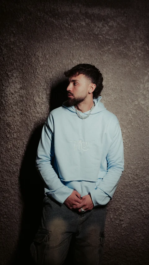 Portrait in a light-blue hoodie in front of a textured wall.