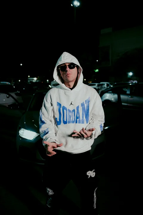 Night portrait in a white hoodie beside a car.