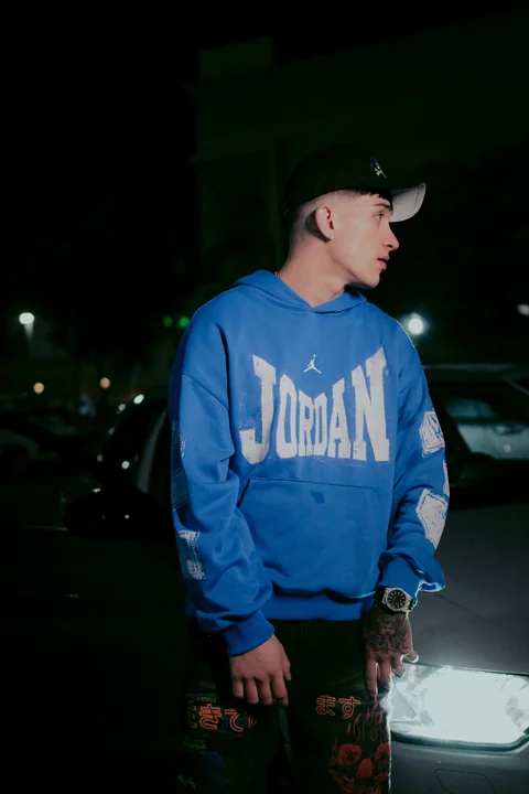 Profile portrait in a blue hoodie with lights in the background.