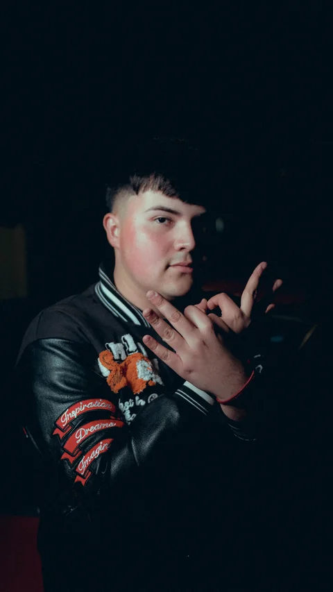 Night portrait in an embroidered jacket with a hand beside the face.