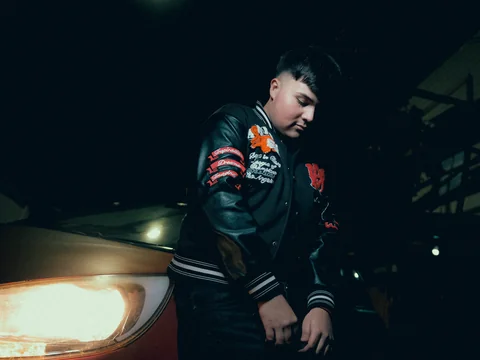 Person in an embroidered jacket beside a car headlight.