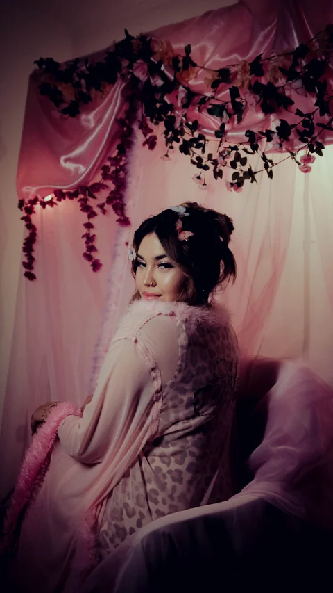 Seated portrait among fabric and pink flowers.