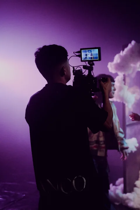 Camera and film crew in front of a cloud set.