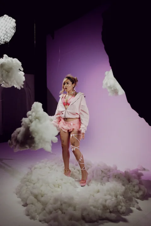 Full-length portrait among prop clouds and violet light.
