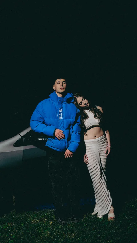 Two people beside a white car at night.