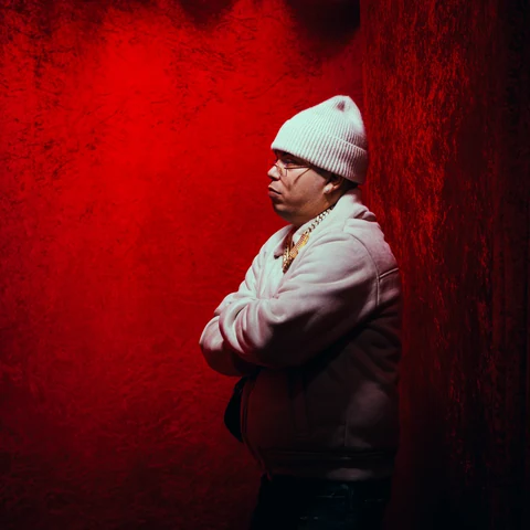 Persona con gorro blanco y brazos cruzados frente a una pared roja.