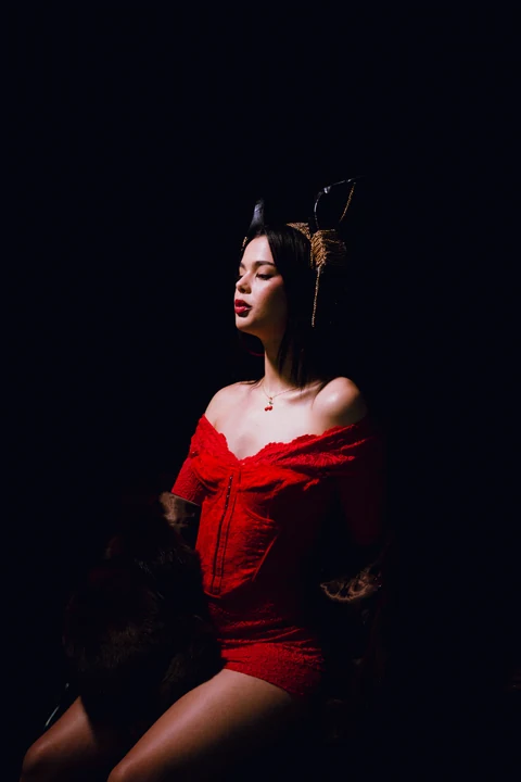 Mujer con vestido rojo iluminada de perfil sobre fondo oscuro.