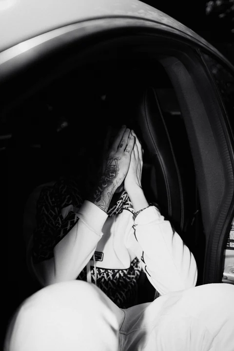 Fotografía en blanco y negro de una persona cubriéndose el rostro dentro de un automóvil.