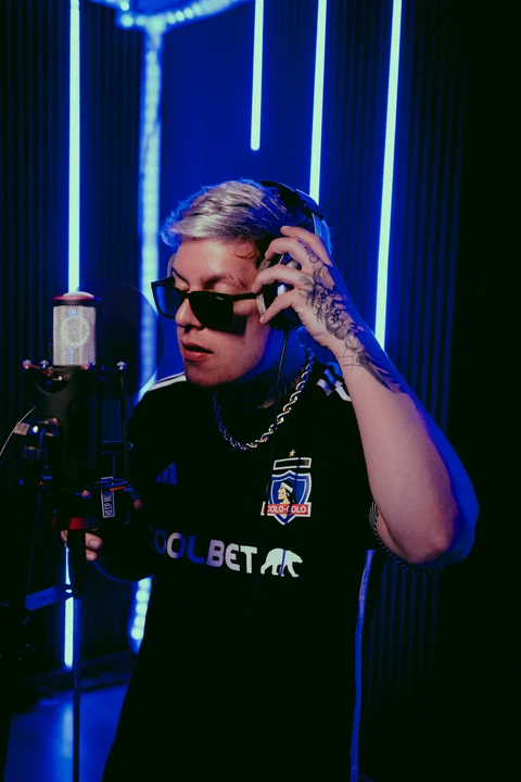 Intérprete con auriculares frente a un micrófono en un estudio con luces azules.