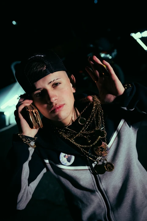 Persona con gorra y cadenas sosteniendo un teléfono junto al rostro de noche.