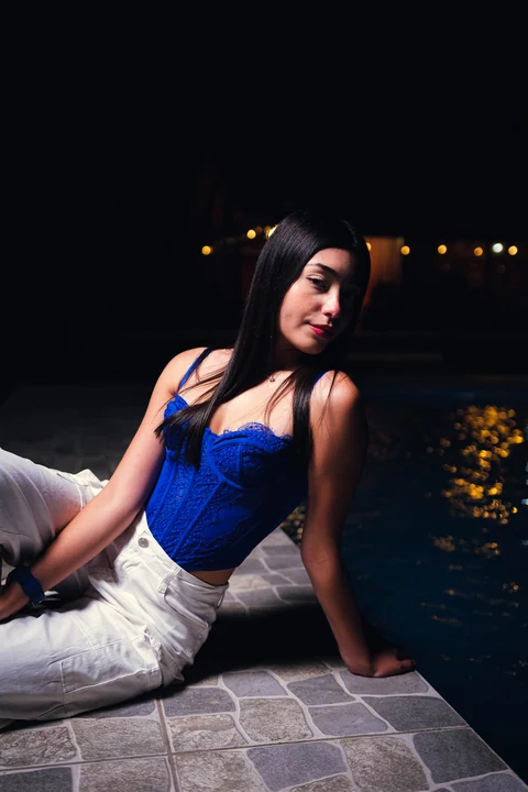 Mujer con top azul sentada junto al agua iluminada de noche.