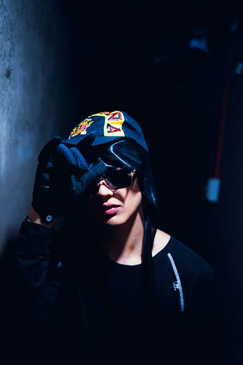 Persona con gorra y gafas oscuras bajo una luz azul lateral.