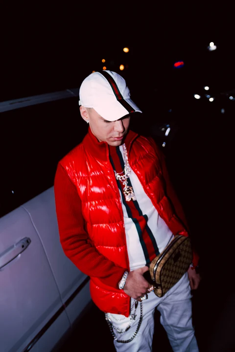 Persona con chaleco rojo apoyada junto a un automóvil de noche.