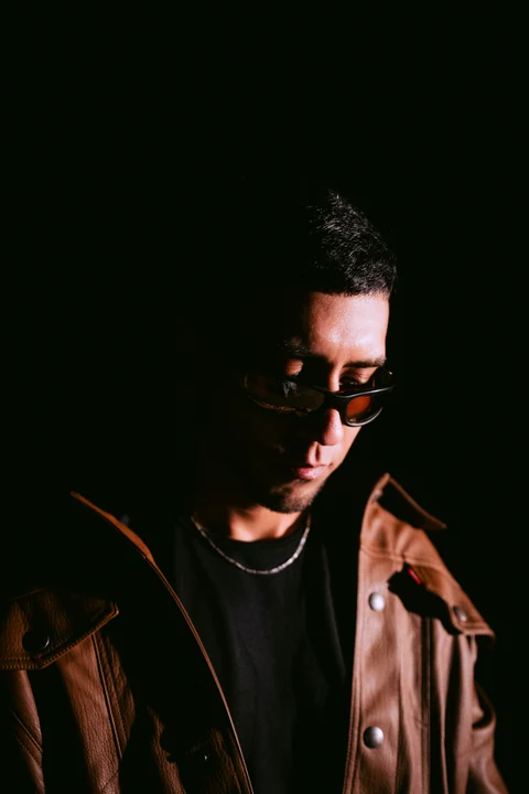Primer plano de una persona con gafas y chaqueta marrón bajo luz lateral.