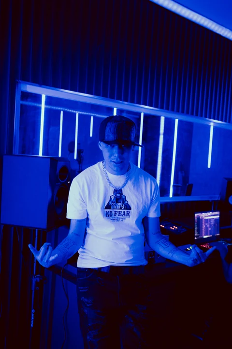 Intérprete con camiseta blanca en un estudio con líneas de luz azul.