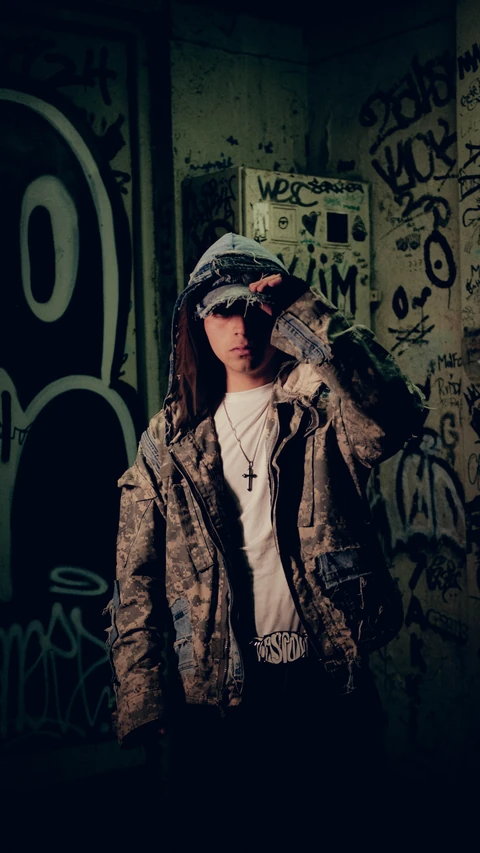 Retrato de una persona con chaqueta de camuflaje junto a un muro con grafitis.