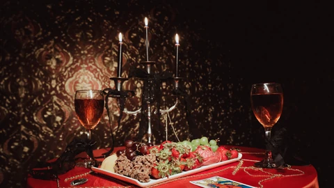 Mesa roja con fruta, copas y un candelabro frente a un fondo dorado.