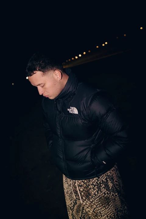 Retrato nocturno de una persona con chaqueta negra mirando hacia abajo.