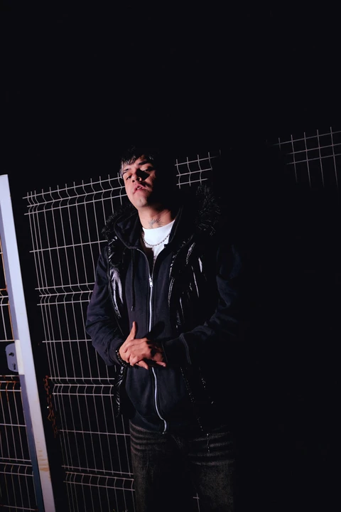 Retrato nocturno de una persona con chaqueta oscura junto a una reja.