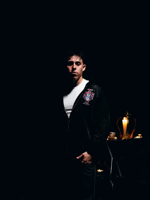 Persona con chaqueta negra en un set oscuro iluminado con velas.