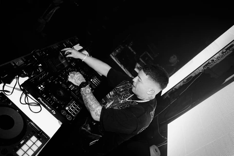 Fotografía en blanco y negro de un DJ junto a su mesa de mezclas.