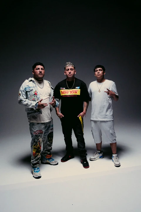 Tres artistas de pie en un estudio con fondo gris y luz cenital.